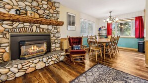 A stone fireplace, wooden dining table, and chairs in a room with wooden flooring and a patterned rug.