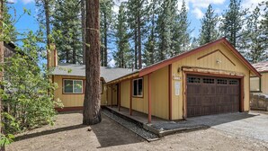 A yellow building with a brown garage door, a small porch, and a tree in front.