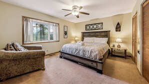 A bedroom with a bed, a chair, a nightstand, a ceiling fan, and a window.