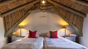 A room with two beds, each with white bedding and red pillows, under a sloped wooden ceiling with exposed beams. There are two bedside lamps on wooden nightstands. - Thatched Apartment with great views, full kitchen, Wifi in Noordhoek, Cape Town (Cape Town)