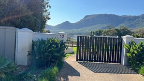 A gated entrance with a number '12' sign, surrounded by lush greenery and a mountainous backdrop. - Thatched Apartment with great views, full kitchen, Wifi in Noordhoek, Cape Town (Cape Town)
