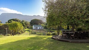 A grassy backyard with a dining area and a house in the background. - Thatched Apartment with great views, full kitchen, Wifi in Noordhoek, Cape Town (Cape Town)
