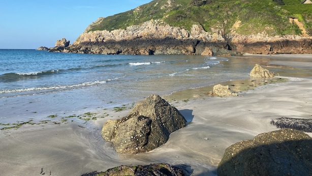 A beach with clear water, large rocks, and a green hillside in the background. - No22 (Barnstaple)