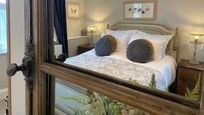 A bedroom with a large mirror, a bed with white linens, two decorative pillows, a wooden headboard, and a framed artwork on the wall. - No22 (Barnstaple)