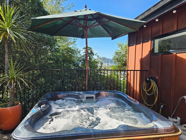 Un jacuzzi con un paraguas verde, rodeado de plantas en macetas y una valla de madera.