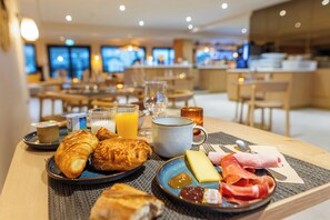 Un desayuno con cruasanes, queso, jamón y jugo sobre una mesa en el comedor de un hotel.