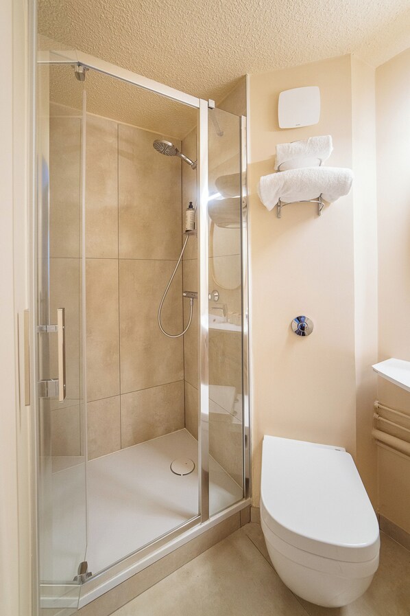 Un baño con ducha envuelta en vidrio, inodoro blanco y un perchero con toallas.