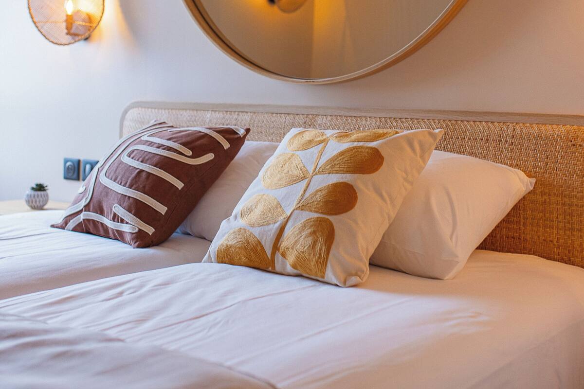 A hotel room with a large round mirror, a bed with white bedding, and a wall-mounted light fixture.