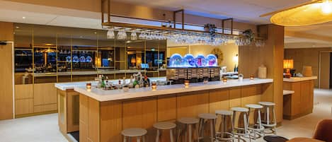 A modern bar area with a long counter, multiple stools, and a seating area with a sofa and tables.