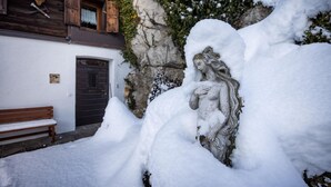 A snow-covered statue in front of a building with a wooden door and a bench.