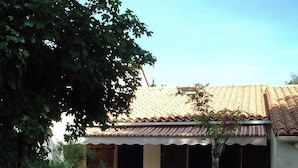 A house with a tiled roof, a patio with white plastic chairs, and a small tree.
