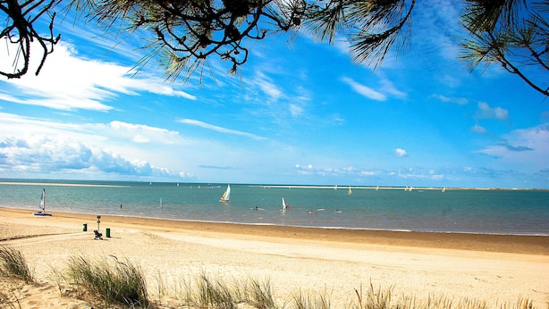 A beach with clear skies, sandy shore, and sailboats in the water.