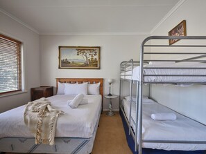 Quarto com uma cama de solteiro, mesa de cabeceira, luminária, um quadro na parede e uma cama beliche.