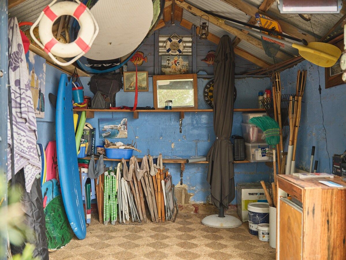 Een rommelige kamer met diverse spullen, waaronder een reddingsboei, surfplanken en schoonmaakspullen.