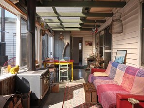 A cozy room with a wooden ceiling, a colorful sofa, a table, and a chair. - Warraburra Beach Shack, Rosebud (Rosebud)