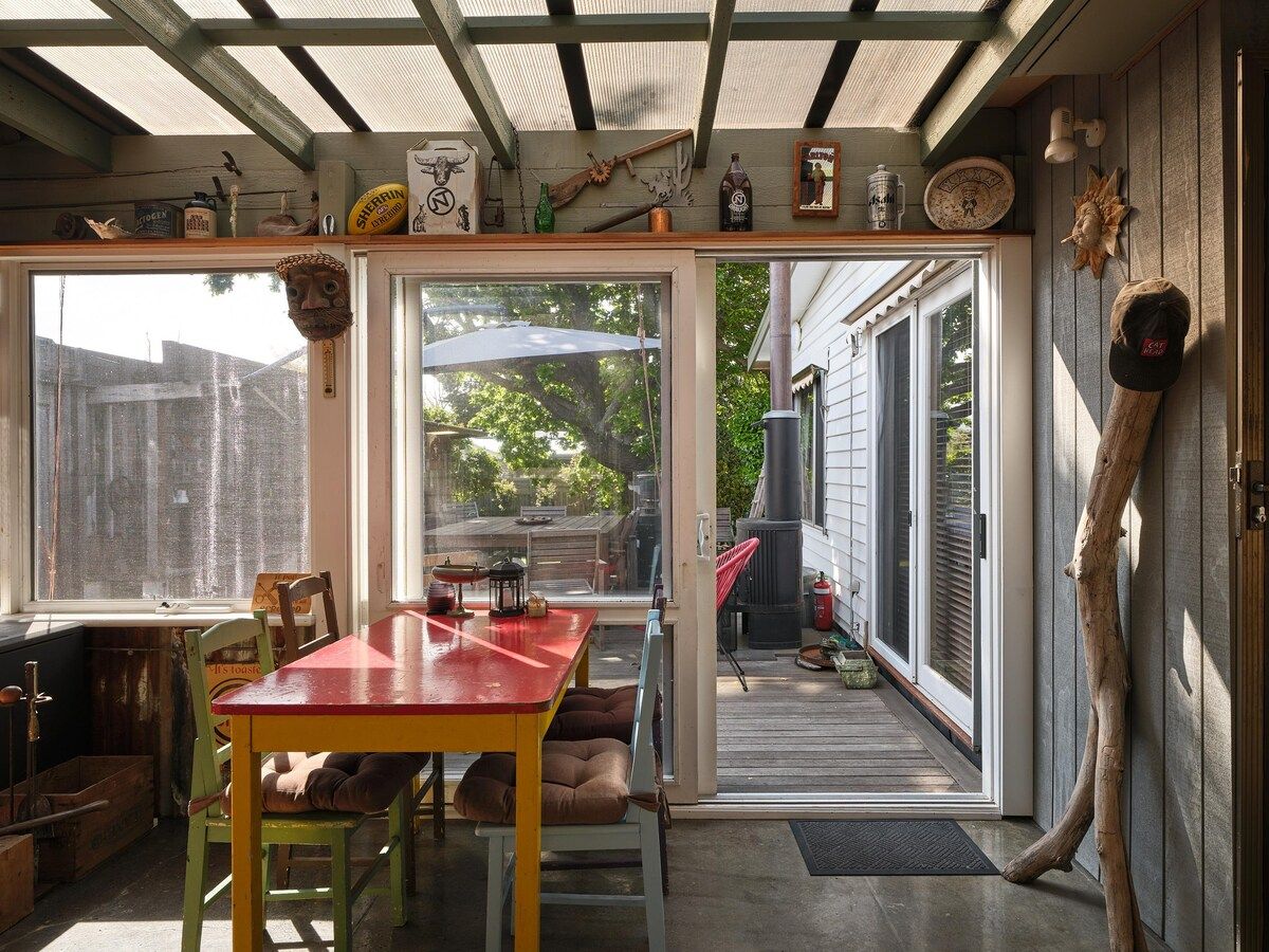 Eine überdachte Terrasse mit Tisch und Stühlen, ein Holzdeck und Blick auf den Garten.