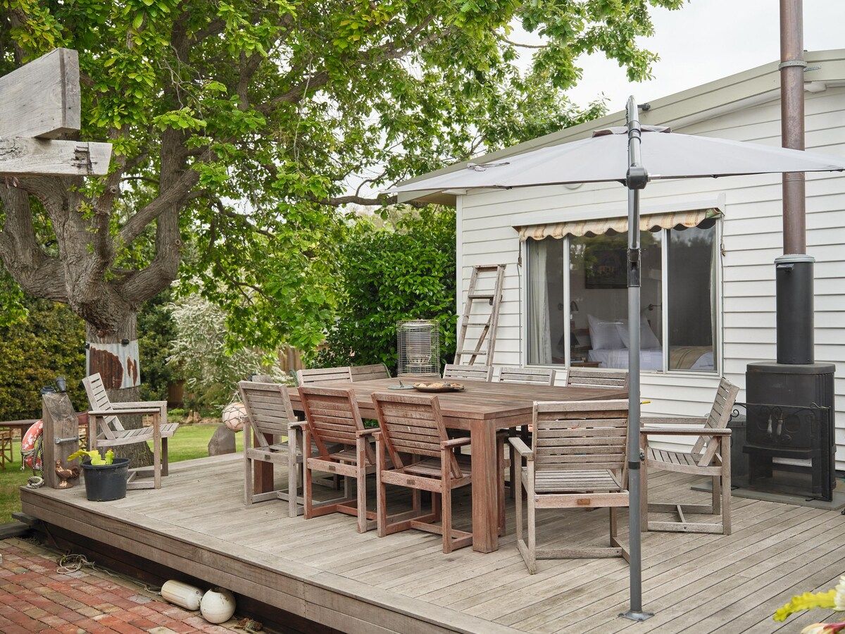 A wooden deck with a table and chairs, a chimney, and a ladder leading to a house.