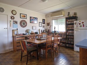 Uma cozinha com mesa de jantar, cadeiras, estante e geladeira.