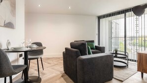 Una sala de estar moderna con una mesa de comedor redonda, asientos tapizados en gris y un amplio ventanal con vista a la ciudad.