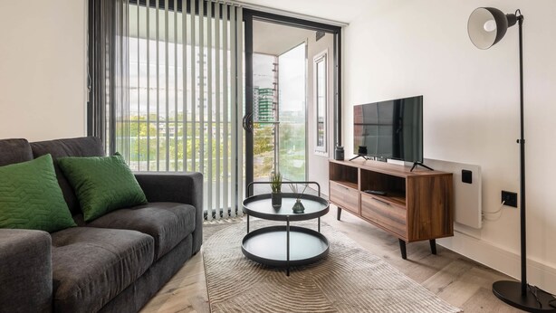 Una sala de estar moderna con un sofá, una mesa de centro de dos niveles, un televisor y una lámpara de pie.