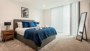 Ein modernes Schlafzimmer mit einem großen Bett, einem Nachttisch, einem Spiegel und einem Fenster mit Jalousien.