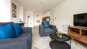 Ein modernes Wohnzimmer mit einem grauen Sofa, einem blauen Sessel und einem Fernseher auf einem Holzgestell.