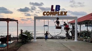 A beachside entrance with a swing set and a sign reading 'LB COMPLEX'.