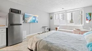 A compact bedroom with a bed, a small desk, a microwave, and a TV. - One Step to The Beach (Sunny Isles)
