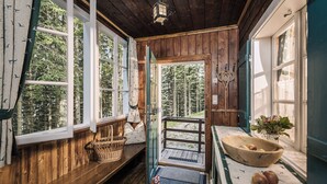 Una cabaña de madera con un banco, una cesta, un cuenco de madera lleno de manzanas y una puerta que da a un bosque.