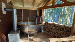 Una sala de sauna con una tina de madera grande, un calentador metálico y una pila de leña.