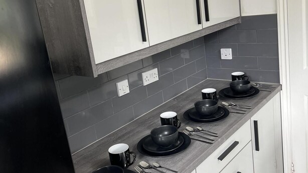 A kitchen with grey tiles, white cabinets, and black appliances. - Cozy 3 Bedrooms Birmingham House With Pool Table (Birmingham)