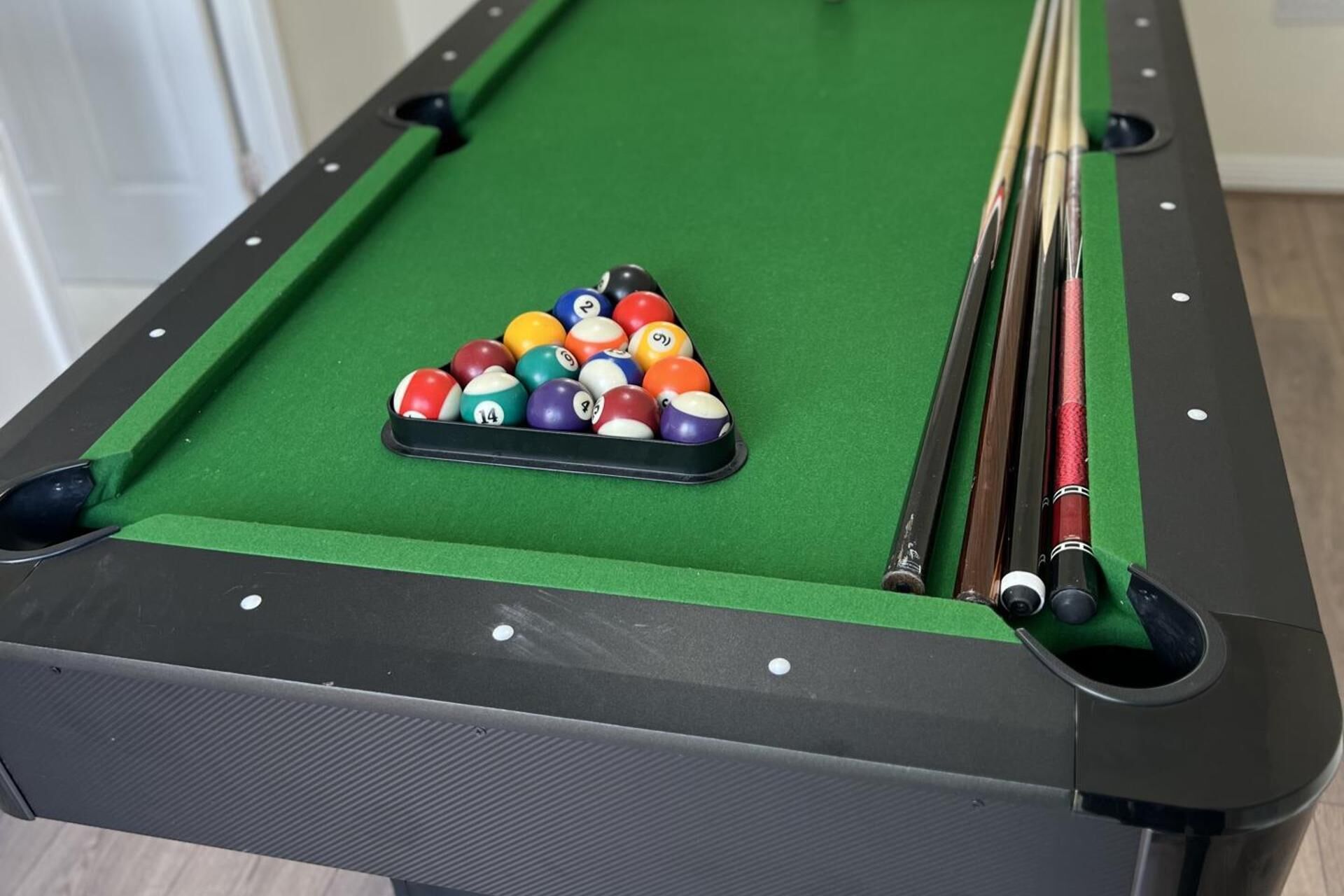 A pool table with a triangular arrangement of billiard balls, pool cues, and a visible pocket.