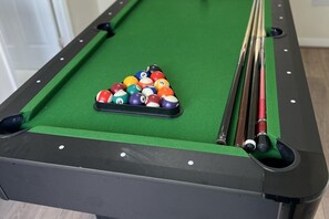 Een pooltafel met een driehoekige opstelling van biljartballen, keu en een zichtbaar gat.