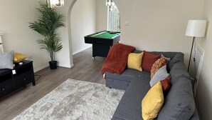 A modern living room with a grey sectional sofa, a pool table, a potted plant, and a chandelier. - Cozy 3 Bedrooms Birmingham House With Pool Table (Birmingham)