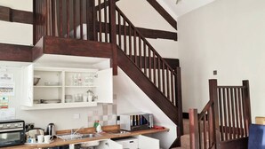 A compact kitchen with a built-in oven, microwave, and a small refrigerator. A wooden staircase leads to a loft area with a bunk bed. - Stay Norwich Apartments Lodge 6 (Norwich)