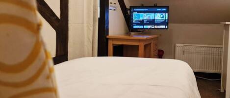 A bedroom with a bed, a remote control, a television on a stand, and a small wooden table.