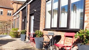 A brick building with large windows and a paved patio area with outdoor seating. - Stay Norwich Apartments Lodge 6 (Norwich)