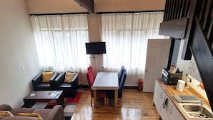 A compact living space with a sofa, a dining table, a kitchen area, and a TV mounted on the wall. - Stay Norwich Apartments Lodge 6 (Norwich)