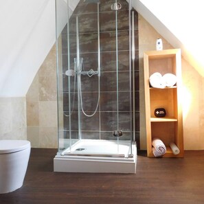A modern bathroom with a glass-enclosed shower, a wooden shelf with toiletries, and a white toilet. - Stay Norwich Apartments City View (Norwich)