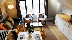 A dining area with a table set for four, surrounded by wooden chairs, a sofa, and a window with curtains.