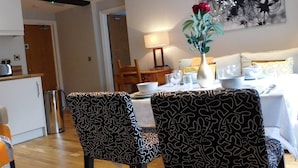 Un comedor con dos sillas estampadas, una mesa dispuesta para cuatro personas y un jarrón con una rosa roja.