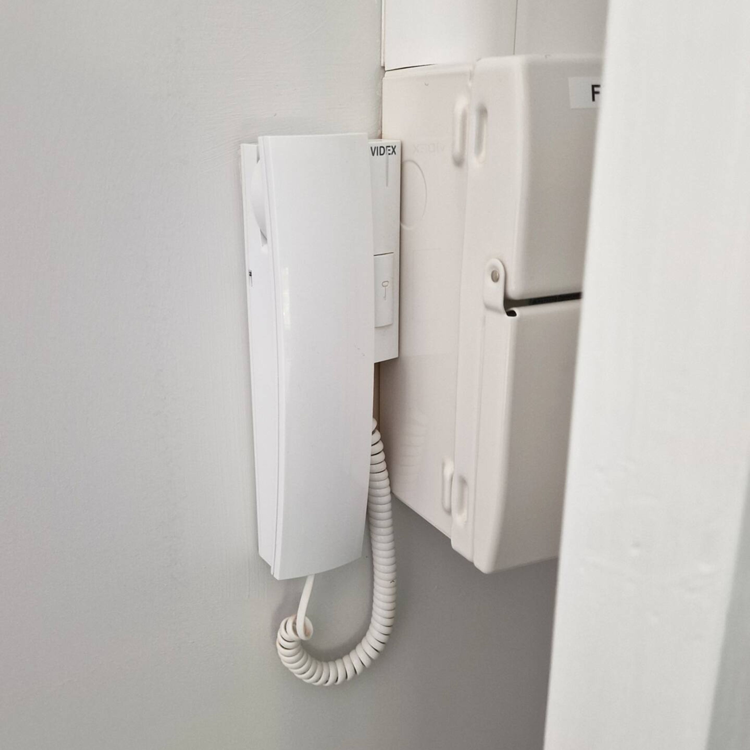 Un téléphone blanc fixé au mur, à côté d’un réfrigérateur.