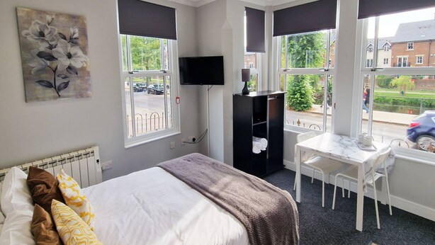 A bedroom with a bed, a desk, a chair, a TV, and a window with a view of the outside. - Stay Norwich Apartments Riverside House Apart-1 (Norwich)
