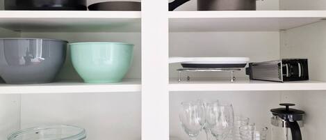 A kitchen with white cabinets, black and grey pots, a green bowl, a grater, and clear glassware.