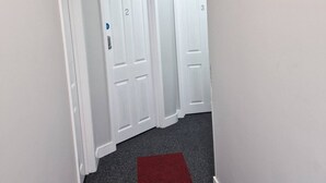 A narrow hallway with white walls and a red carpet. There are three white doors, each marked with a number. - Stay Norwich Apartments Riverside House Apart-1 (Norwich)