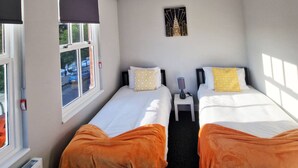 A hotel room with two beds, a small table, a nightstand, a wall-mounted picture, and a window with a view of the outside.