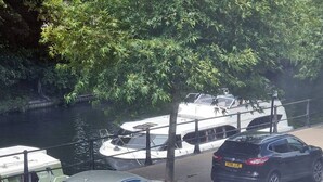 A river with boats docked alongside a road with parked cars.