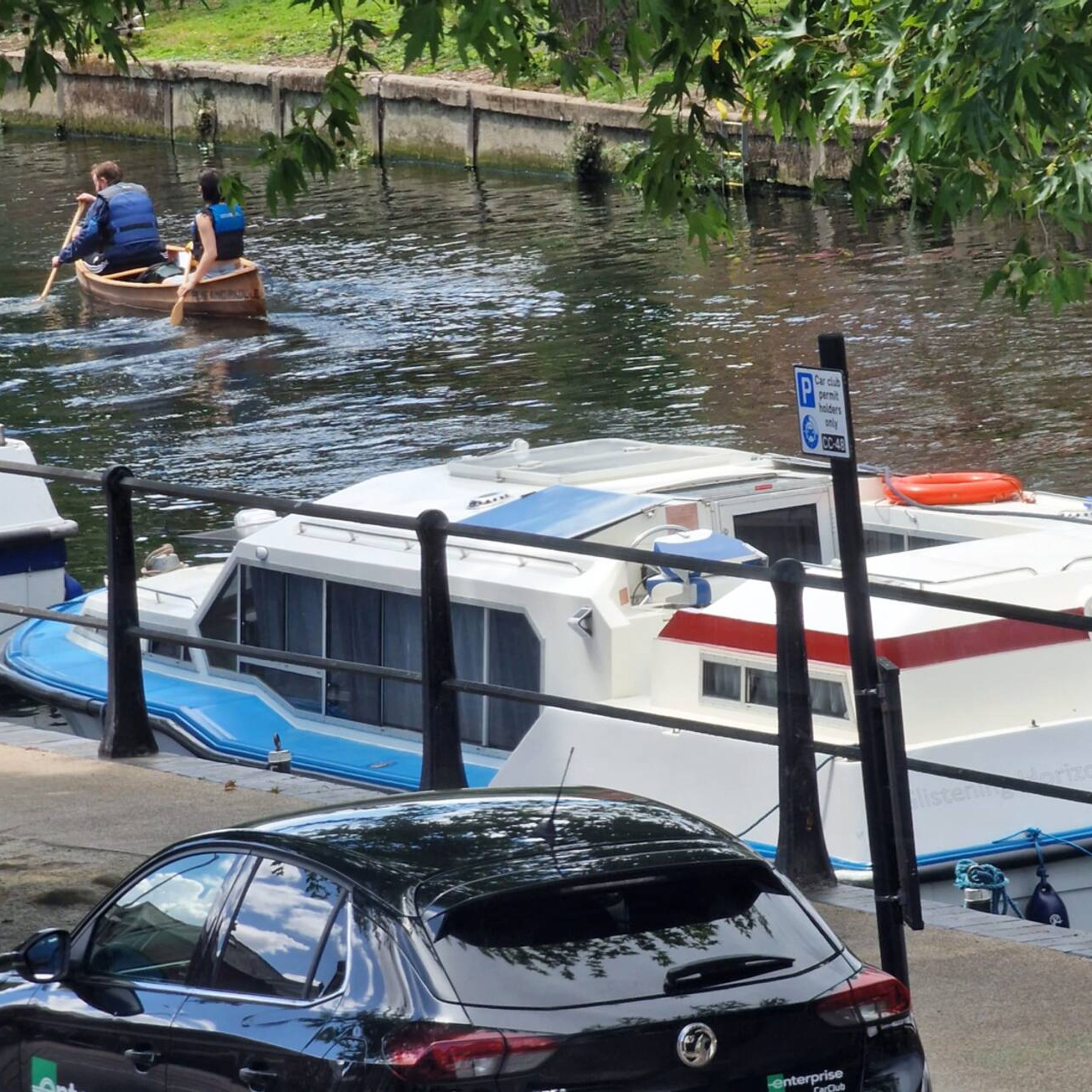 A marina with boats docked, a car parked nearby, and a sign indicating car club permit holders only.