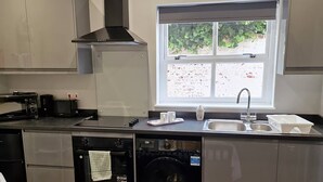 A compact kitchen with a built-in washer and dryer, a window with a view, and a sink with a faucet. - Stay Norwich Apartments Riverside House Apart-3 (Norwich)