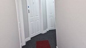A hallway with white doors numbered 2 and 3, a red carpet, and a ceiling-mounted security camera. - Stay Norwich Apartments Riverside House Apart-3 (Norwich)